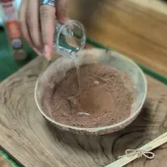 Adding water to incense powder in a coconut bowl