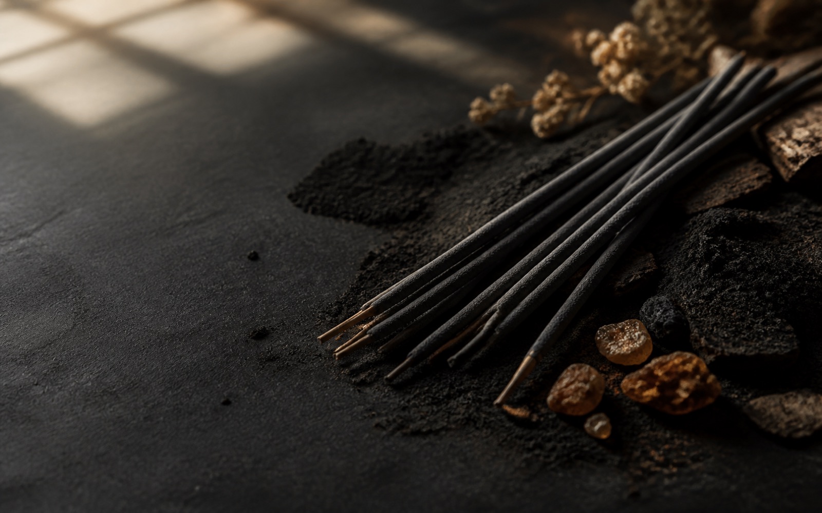 Black incense sticks resting on dark agarwood powder